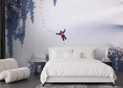 Winter aerial view portrait of Snowboarder female lying in clean snow between Christmas trees. Snowy mountain in ski resort, sunny winter holiday Wall mural