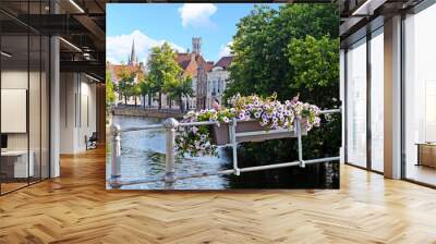 View over Bruges from canal with belfry and church of Our Lady, flower box with violet petunias in the front, blue sky with fluffy white clouds Wall mural