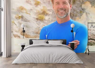 Mature smiling man standing, arms crossed at the beach Wall mural