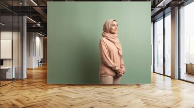 Muslim woman in hijab looking up at copyspace over green background Wall mural