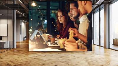 Deadlines wait for no one. Shot of a business team using a laptop together on a night shift at work. Wall mural