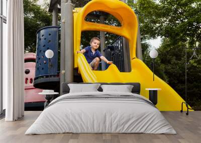 Low angle view of cute three-year old boy in casual clothes climbing on yellow slide in children playground, Montreal, Quebec, Canada  Wall mural