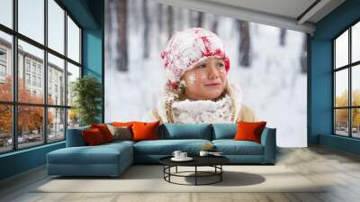 Crying girl wearing in red knitted hat in snowy winter park. Little sad child play with snow in forest. Family winter vacation with  kid. Young girl froze and cry Wall mural