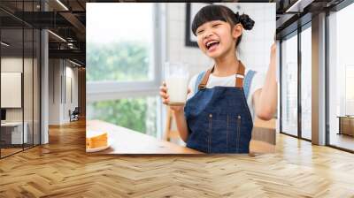 Asian little cute kid holding a cup of milk in kitchen in house. Young preschool child girl  stay home with smiling face, drinking milk and then look at camera.Milk for good health. Wall mural