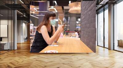 Asian woman sitting separated in restaurant eating food .keep social distance for protect infection from coronavirus covid-19, restaurant and social distancing concept. Wall mural