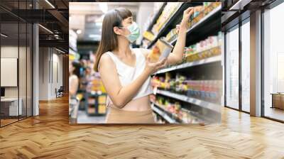 Asian woman wearing face mask push shopping cart in suppermarket . Girl choosing, looking somethings to buy at shelf during coronavirus crisis or covid19 .happy lifestyle or shopaholic concept. Wall mural