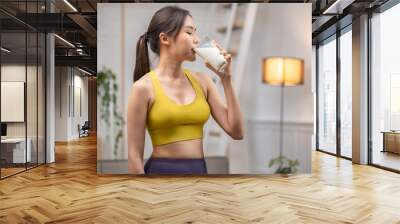 Attractive fitness asian woman finishing workout and drinking protein milk shake vitamins after training at home. Bodybuilding. Healthy lifestyle. Wall mural