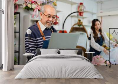 Elder senior man florist talking on smartphone using laptop at florist.portrait of mature male small business owner using laptop and looking at camera in flower shop Wall mural