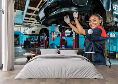 Engineer team checking under car condition on lifter in garage.Young auto mechanic in uniform is looking at camera and smiling examining car... Wall mural