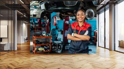 Engineer team checking under car condition on lifter in garage.Young auto mechanic in uniform is looking at camera and smiling examining car... Wall mural