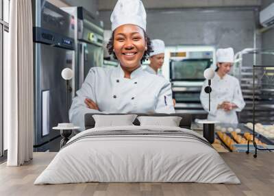 Smiling african  female bakers looking at camera..Chefs  baker in a chef dress and hat, cooking together in kitchen.Team of professional cooks in uniform preparing meals  in the kitchen. Wall mural