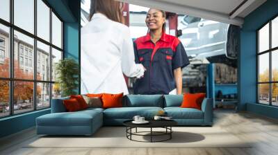 woman receiving her car keys.young african woman engineer auto mechanic in uniform is returning car key to a client, both are smiling. Wall mural