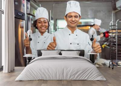 Young  African  female and  senior asian male bakers looking at camera..Chefs  baker in a chef dress and hat, cooking together in kitchen.Team of professional cooks in uniform. Wall mural