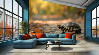 a small turtle rests on the ground surrounded by a brown leaf and a blurry tree Wall mural