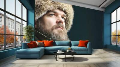 A bearded man in a warm fur hat gazes thoughtfully into the distance, showcasing the essence of winter style and rustic allure in a cozy, inviting atmosphere Wall mural