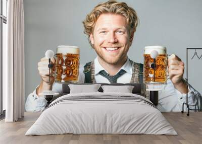 A cheerful blond man dressed in traditional Bavarian costume proudly holds two frothy mugs of beer, embodying the festive spirit of Oktoberfest Wall mural