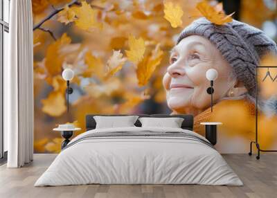 Elderly woman smiling in autumn park as leaves fall around her, enjoying nature's beauty in a vibrant setting filled with orange foliage Wall mural