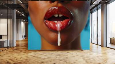 Close-up of a woman's lips with a drop of milk dripping down, set against a blue background. Wall mural