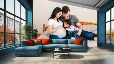  Family Asian Chinese pregnant woman and Caucasian man with toddler girl sitting on bed at home. Mother, father and baby daughter expecting waiting for a new family member. Ethnic diversity. Wall mural