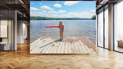 Caucasian preschool blonde girl in pink swimsuit standing on wooden lake river dock with pool noodle on bright sunny summer day. Happy healthy active lifestyle childhood. Wall mural