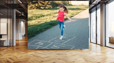 Cute adorable little young child girl playing hopscotch outdoors. Funny activity game for kids on playground outside. Summer backyard street sport for children. Happy childhood lifestyle. Wall mural