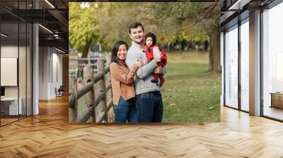 Happy Halloween. Smiling Asian Chinese mother and Caucasian father dad with baby girl in ladybug Halloween costume. Ethnic family in autumn fall park outdoors celebrating holiday. Wall mural