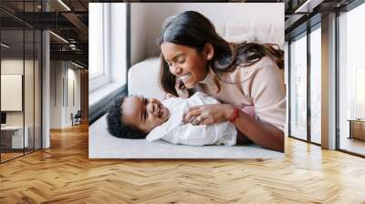 Happy smiling laughing Indian mother playing with black baby girl daughter. Family mixed race people mom and a kid together hugging at home. Authentic candid lifestyle with infant kid child. Wall mural