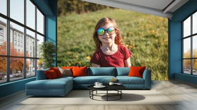 Happy smiling young Caucasian girl in funny sunglasses posing outdoors. Cute adorable kid child having fun outside. Happy childhood lifestyle. Sincere positive emotion. Wall mural