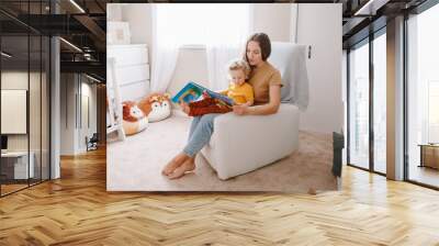 Mom reading book with baby boy toddler at home. Early age children education, development. Mother and child kid spending time together. Family authentic candid lifestyle. Wall mural