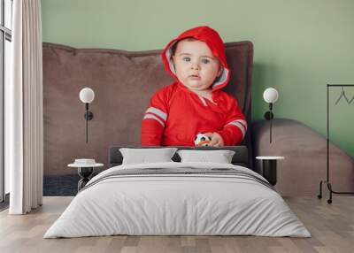 Portrait of cute adorable Caucasian baby boy, wearing red sport hoodie shirt and tracksuit pants. Seven months child sitting on couch and holding football soccer toy Wall mural