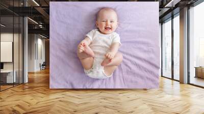 Portrait of cute adorable smiling laughing white Caucasian baby girl boy with blue eyes four months old lying on bed looking at camera. View from top above. Happy childhood lifestyle. Wall mural