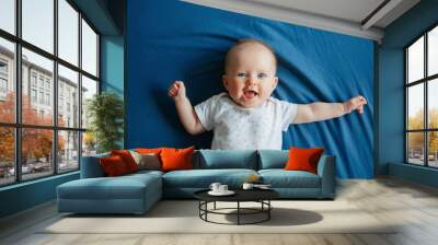 Portrait of cute adorable smiling white Caucasian baby girl boy with blue eyes four months old lying on bed in bedroom looking at camera. View from top above. Happy childhood lifestyle. Wall mural