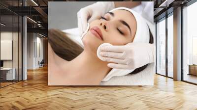 Close up of hands of skillful beautician cleaning and touching female face with cotton pad or sponge. The woman is lying and relaxing. Her eyes are closed with pleasure Wall mural