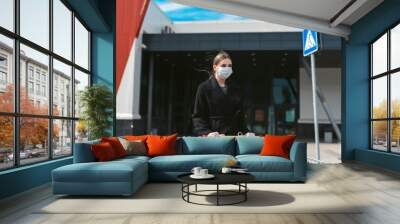 Social distancing during the Coronavirus Covid-19 pandemic. Young woman with a grocery cart on a supermarket background. Disposable mask on face and gloves on hands of a girl. Quarantine shopping Wall mural