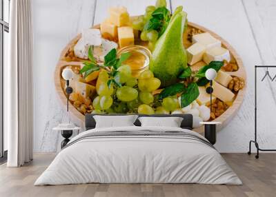 Round wooden platter presenting cheese selection with grapes and pear Wall mural