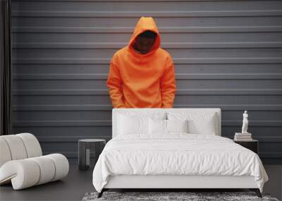 African American man wearing blank orange hoodie standing against grey wall Wall mural