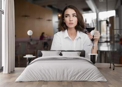 Young woman holding red wine glass sitting in the restaurant Wall mural