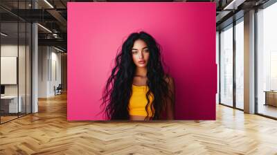 Portrait of an attractive young woman with dark hair, wearing yellow isolated on an pink background, shot in a studio. Wall mural