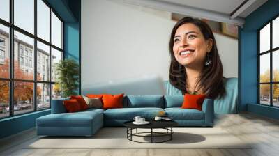 Close up of smiling latin woman looking aside with laptop at home Wall mural