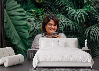 Portrait of a happy woman looking at her social networks on her smartphone outdoors on a background of foliage. Telephone company concept
 Wall mural