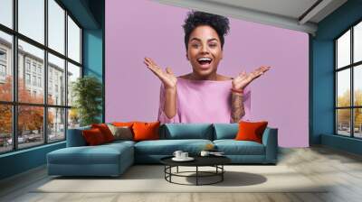 Joyful African American female gestures with hands and exclaimed in happiness, stares at camera, receives unexpected proposal from boyfriend, wears jacket. People and happiness concept. Wall mural