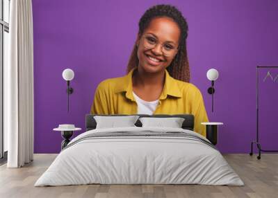 Young cheerful beautiful African American woman student wearing glasses smiling sincerely tilt head to side and look at you dressed in casual style stands on purple plain background Wall mural