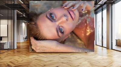 very beautiful woman with incredible blue eyes lies on the golden sand. Sensual portrait of amazing girl wet hair. Tan beach vacation spa. Sexy model portrait close-up. Glamor sparkles on body Wall mural