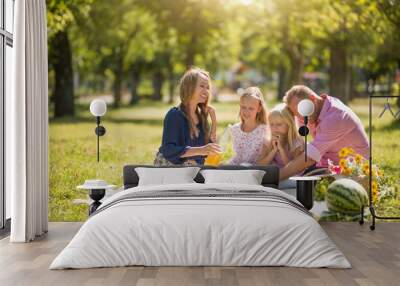 A cheerful family sitting on the grass during a picnic in the park, there is a basket with food and watermelon Wall mural