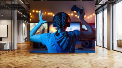 A gamer or a streamer girl at home in a dark room with a gamepad playing with friends on the networks in video games. A young man sits in front of a monitor or TV. Wall mural