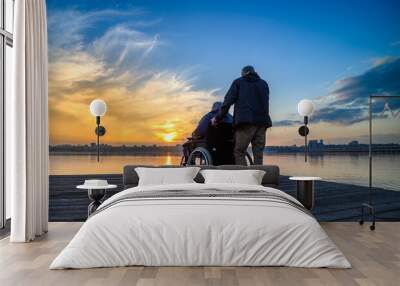 An elderly woman in a wheelchair looks at the sunset on the lake Wall mural