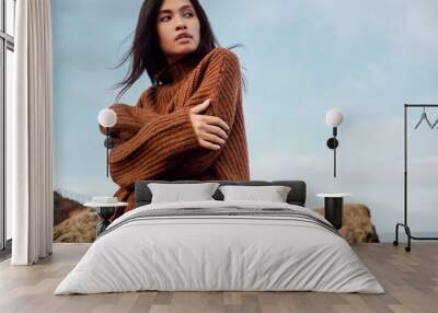 Beautiful casual Asian girl in knitted sweater dreamily looking away by the sea Wall mural