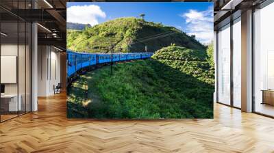 Blue train driving through tea fields Wall mural