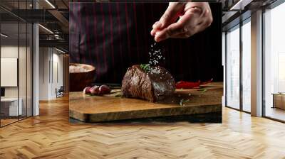 Chef hands cooking meat steak and adding salt and pepper on black copy space background for menu restaurant or recipe text. Wall mural