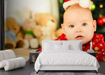 Newborn baby boy in a red Santa hat lies on the bed near the Christmas tree Wall mural